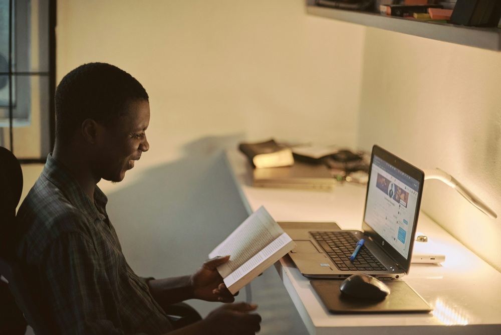 An aspiring prompt engineer enhances his skills through online learning. Many professionals start by experimenting with AI models and studying resources from the comfort of home, blending traditional learning (books) with interactive practice on their laptop.